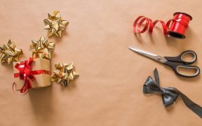 Aprende cómo envolver regalos de Navidad originales. Superficie con lazos y tijeras